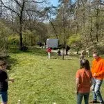 SpeelKubb brengt sport en spel samen op Second Tent Event Instructeur van SpeelKubb legt de spelregels van kubb uit aan kinderen op een grasveld.